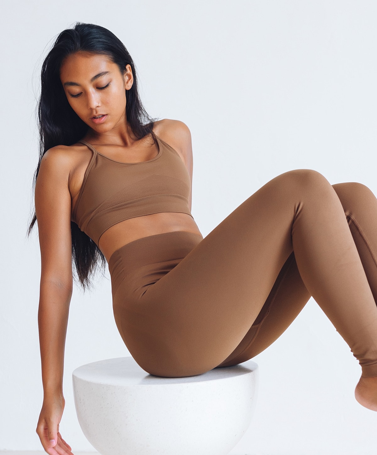 Woman in brown activewear sitting on pedestal.