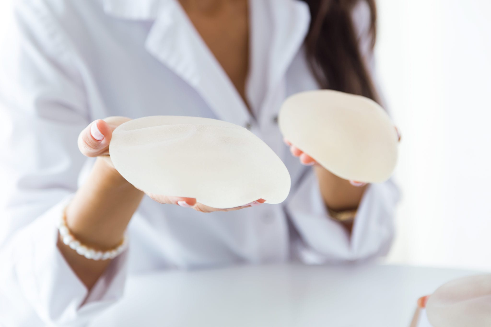 close up picture of woman holding two different types of breast implants