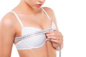 Close up of young woman measuring her bust size with tape measure