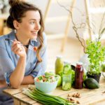 woman eating healthy salad sitting on the table with green fresh ingredients